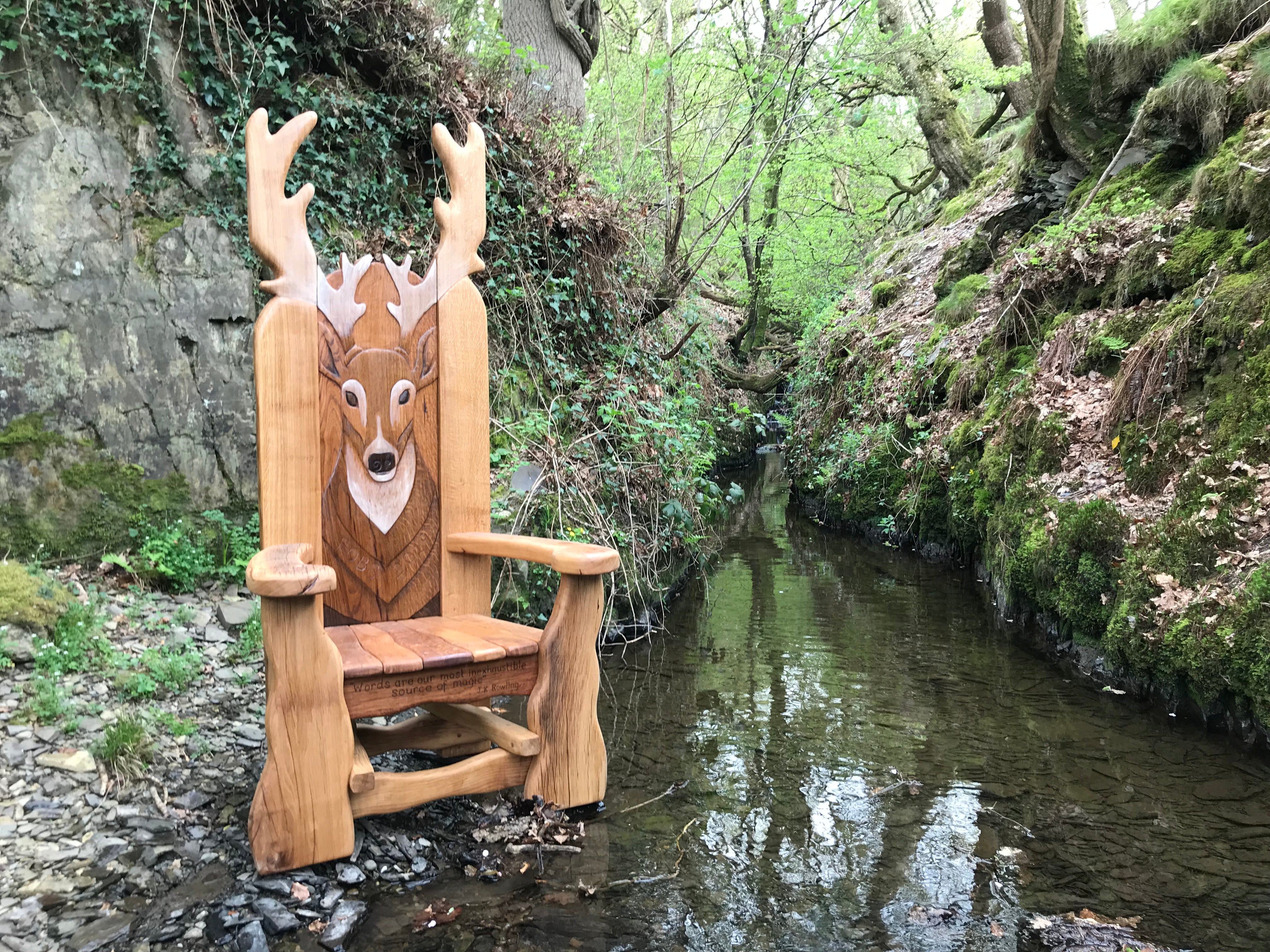 Deer-themed wooden chair by a forest stream.