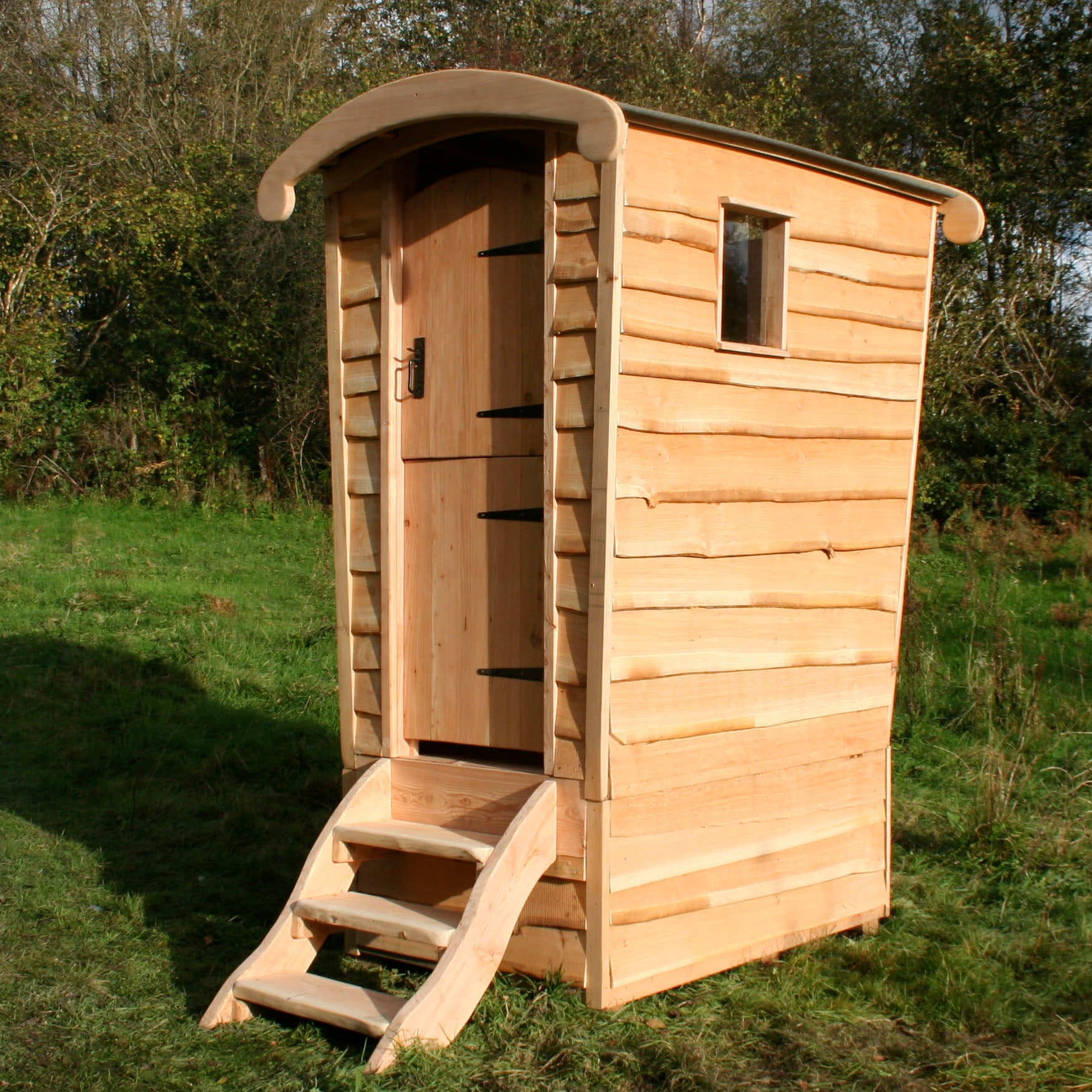 Eco-friendly handcrafted compost toilet by Free Range Designs, featuring a rustic wooden structure with a curved roof and natural cladding, blending seamlessly with outdoor settings for a sustainable and stylish solution.