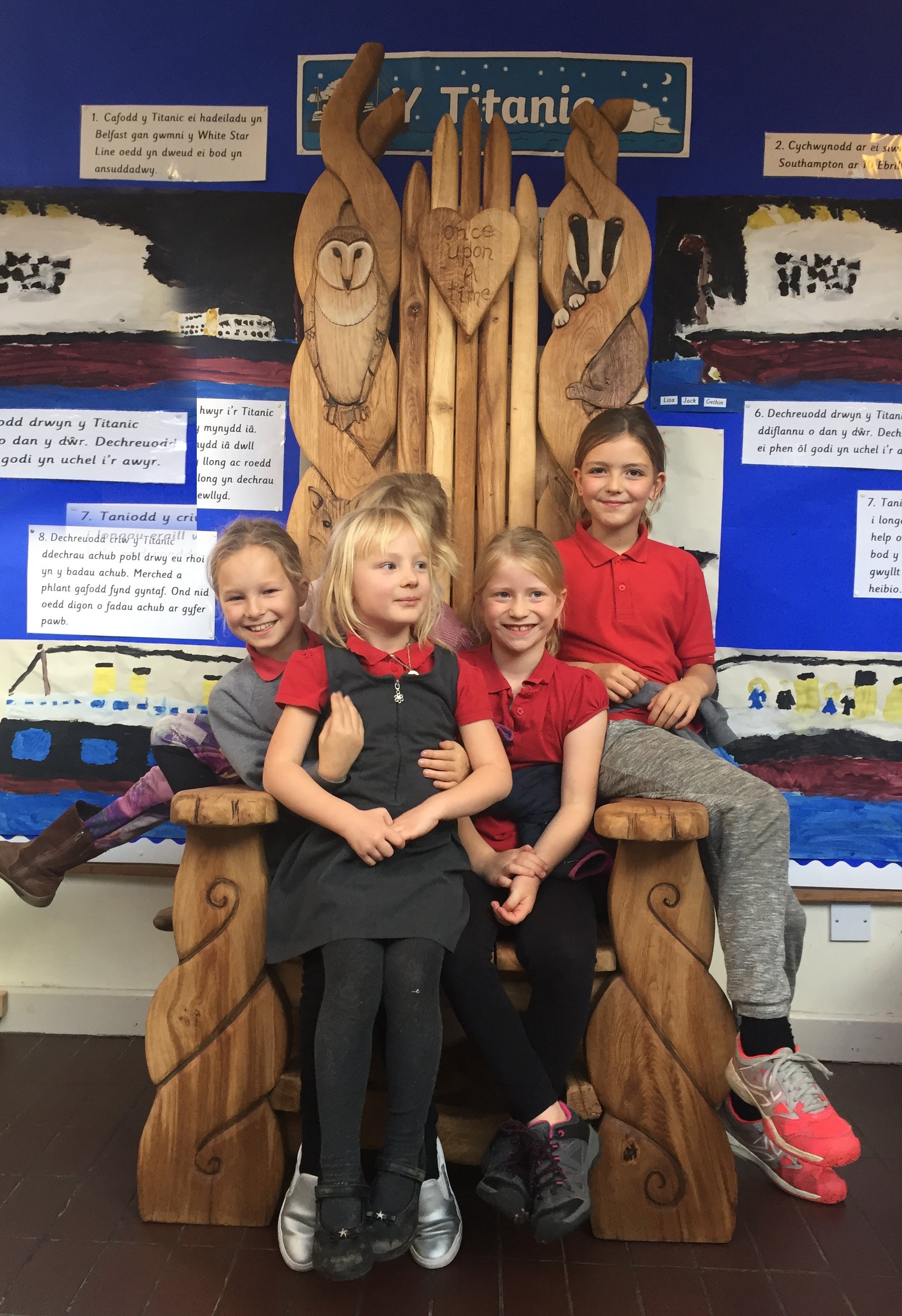 Group of children on a large wooden chair with animal carvings.