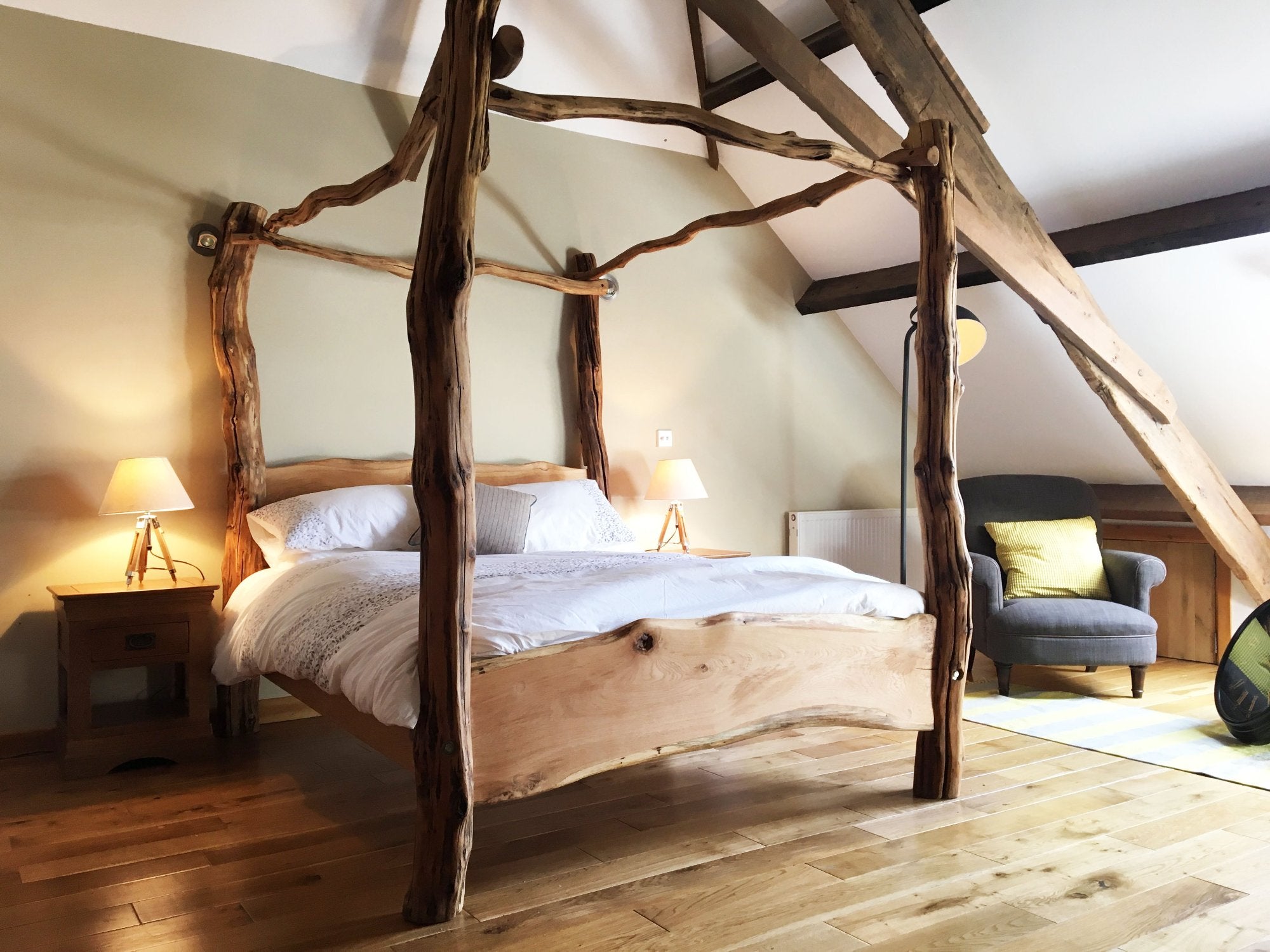 Beautiful handcrafted oak four-poster bed with natural wood features, placed in a cozy attic bedroom with wooden floors and soft lighting, offering a rustic yet elegant ambiance