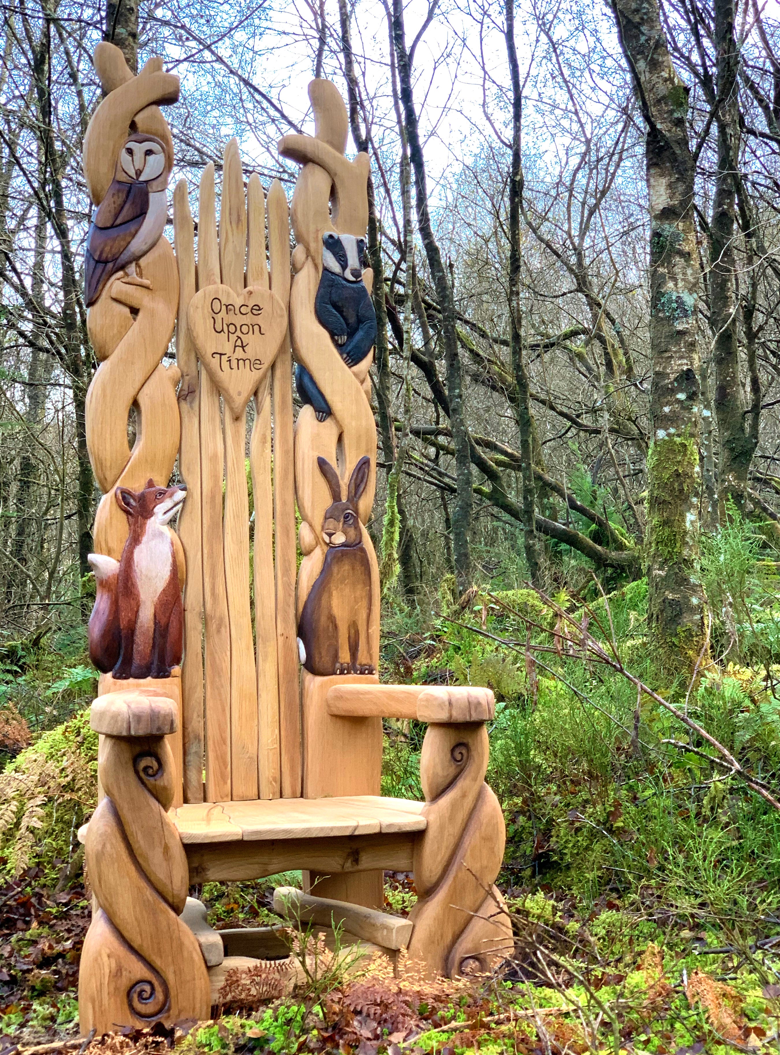 Wooden chair with animal carvings in a wooded area.