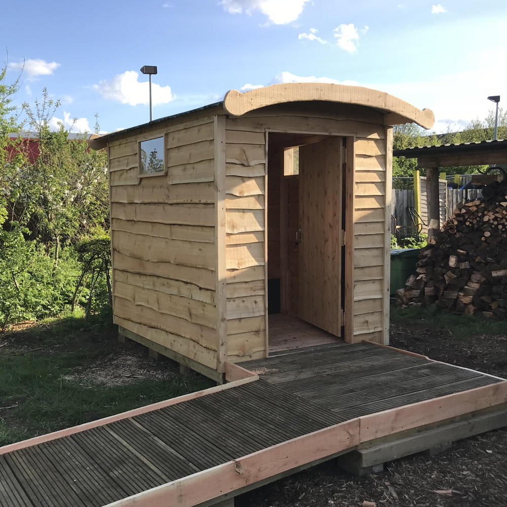 Wooden compost toilet with ramp access in garden setting