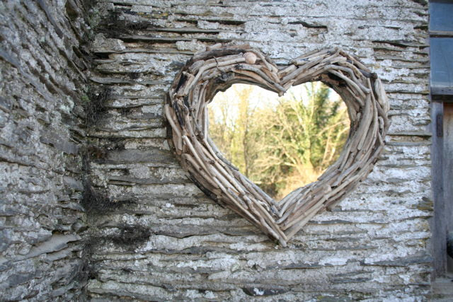 Heart mirror with driftwood frame on stone wall