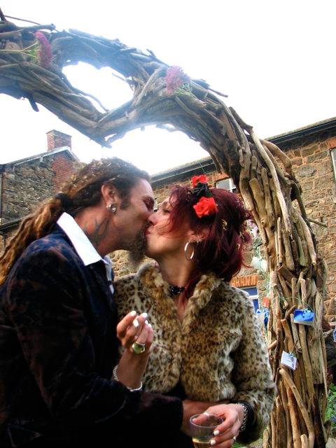 Couple kissing under driftwood wedding arch