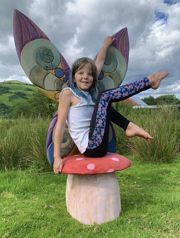 Child sitting on whimsical mushroom fairy chair outdoors