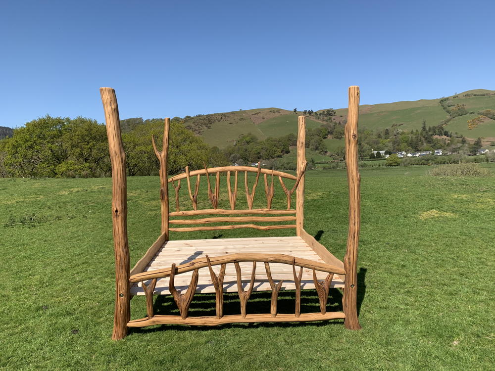 Natural oak four poster bed in green landscape