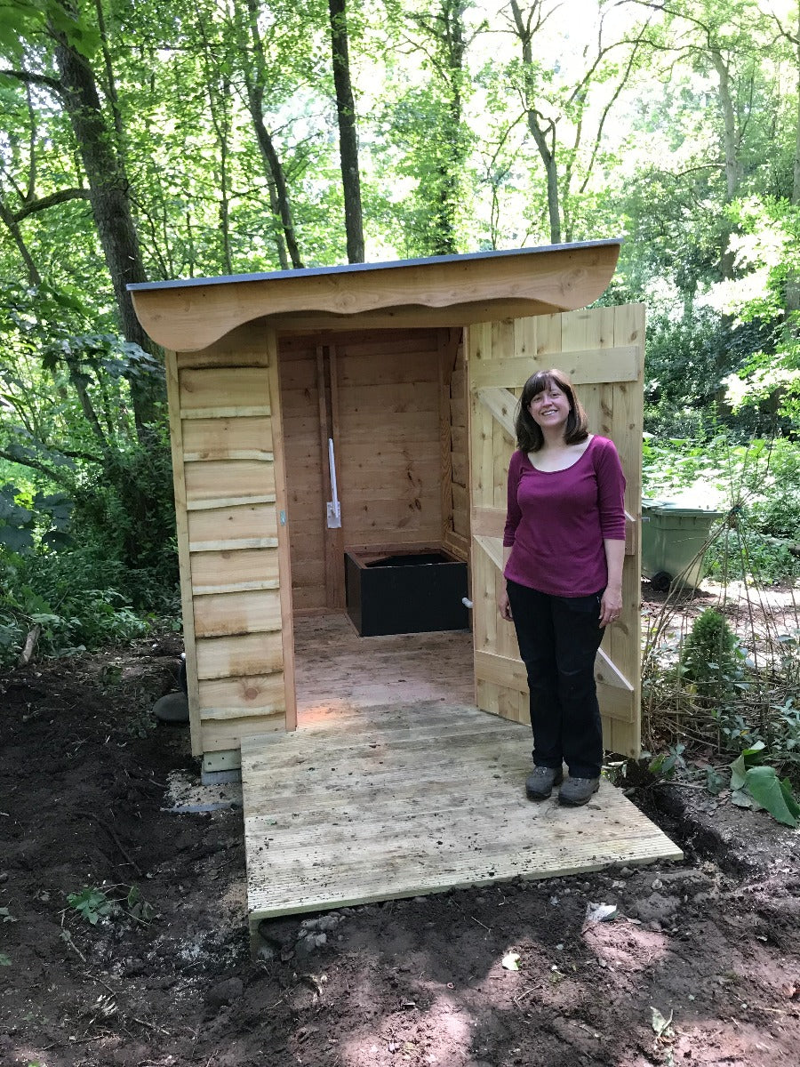 Woman standing in front of a wooden compost toilet